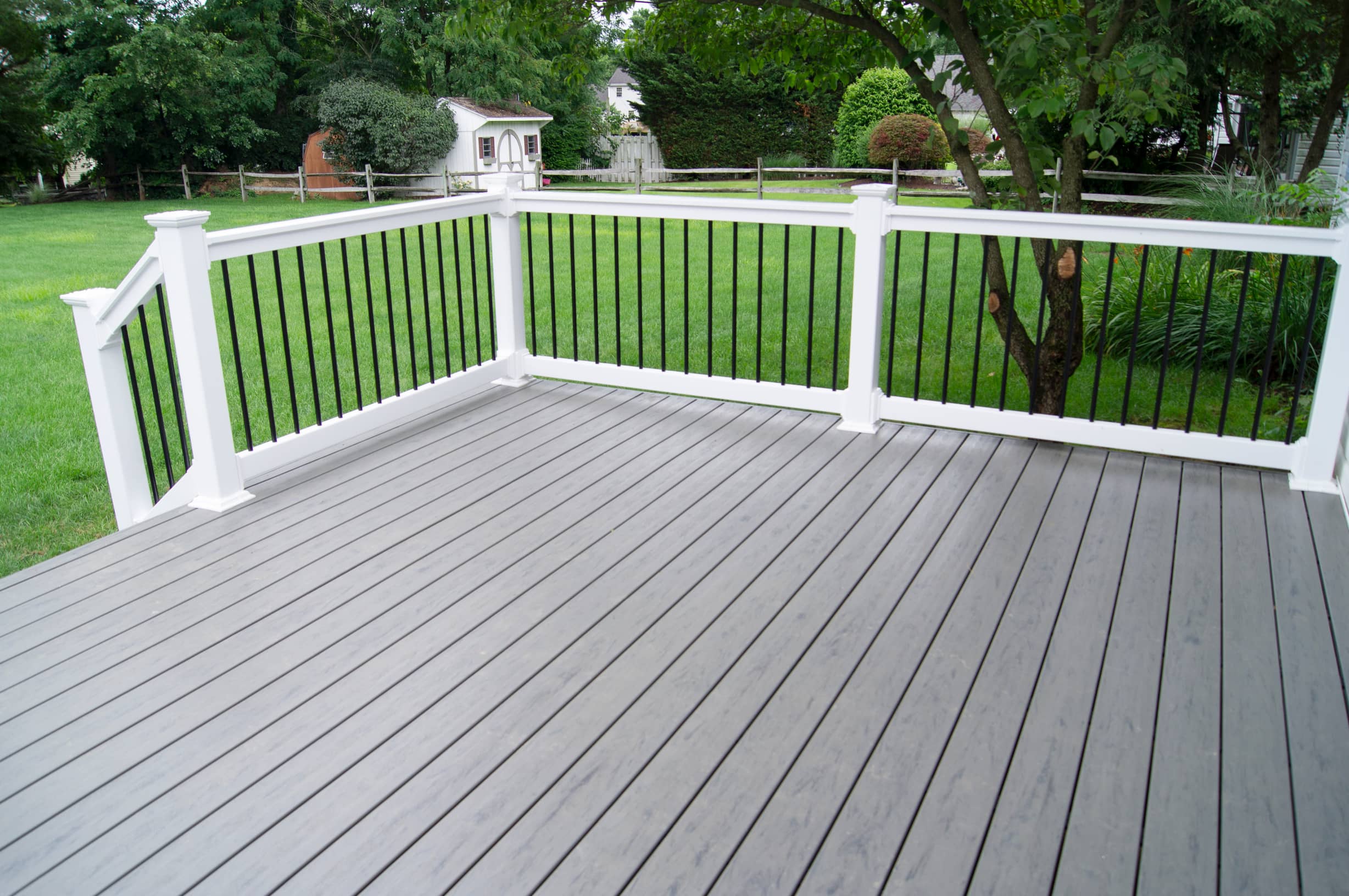 This image is of a gray deck with white railing next to a backyard lawn for a home.