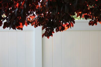 This photo shows a vinyl fence with leaves over the top.