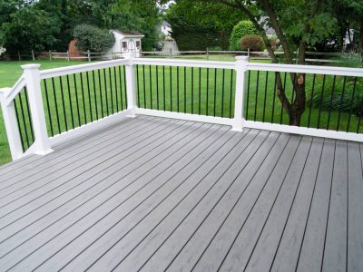 This image is of a gray deck with white railing next to a backyard lawn for a home.